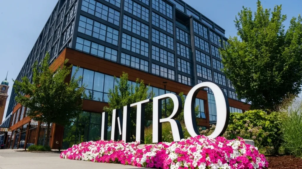 The sculptural INTRO letters at the building entrance on West 25th Street, framed by pink and white petunias